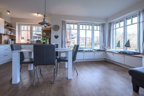 A modern kitchen with white cabinetry, a dining area with a table and chairs, and large windows with views of the outside. - Dune Star Wangerooge (Wangerooge)