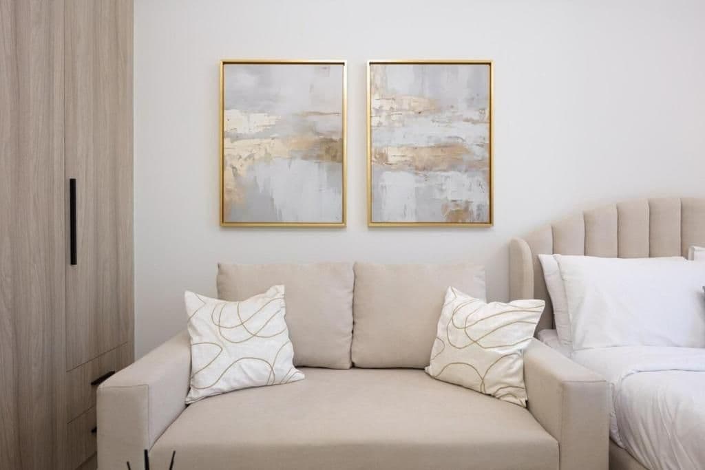 A neutral-toned sofa with patterned cushions, a wooden wardrobe, and two abstract paintings on the wall.