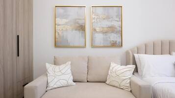 A neutral-toned sofa with patterned cushions, a wooden wardrobe, and two abstract paintings on the wall.