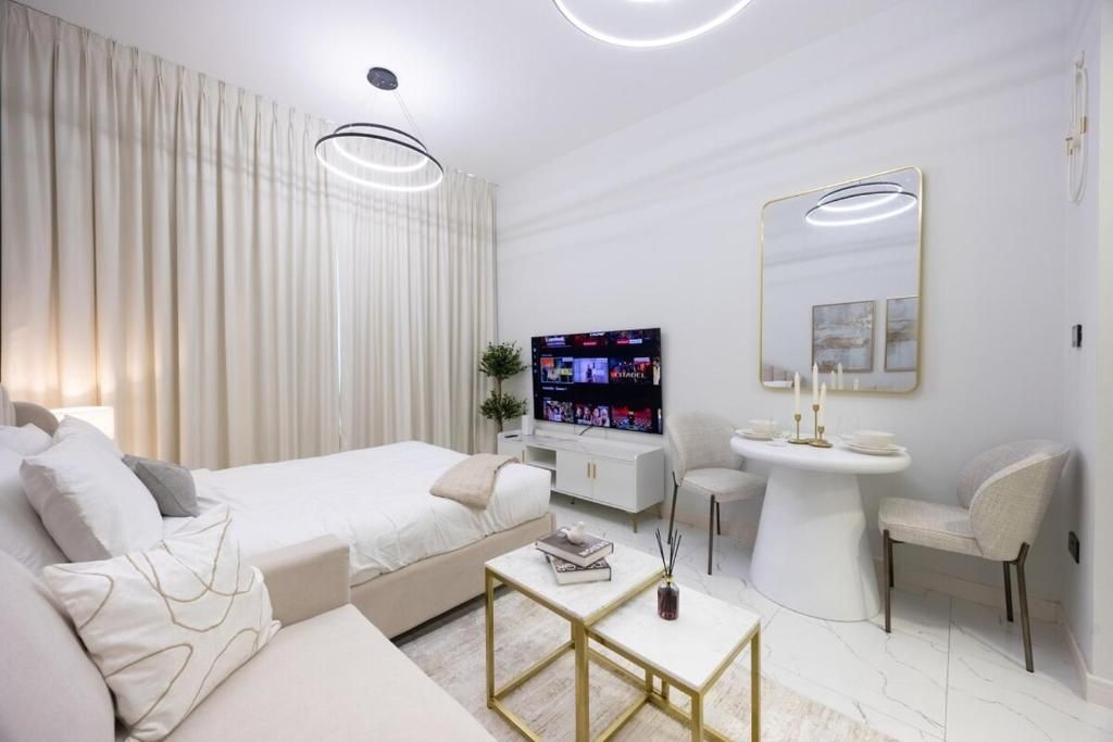 A modern hotel room with a bed, a sofa, a TV, a small table, a mirror, and a bathroom area.