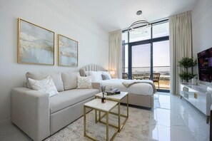 A modern living room with a sofa, a coffee table, and a bed with a view. - Bloomfields Studio in The Gate - Masdar (Abu Dhabi)