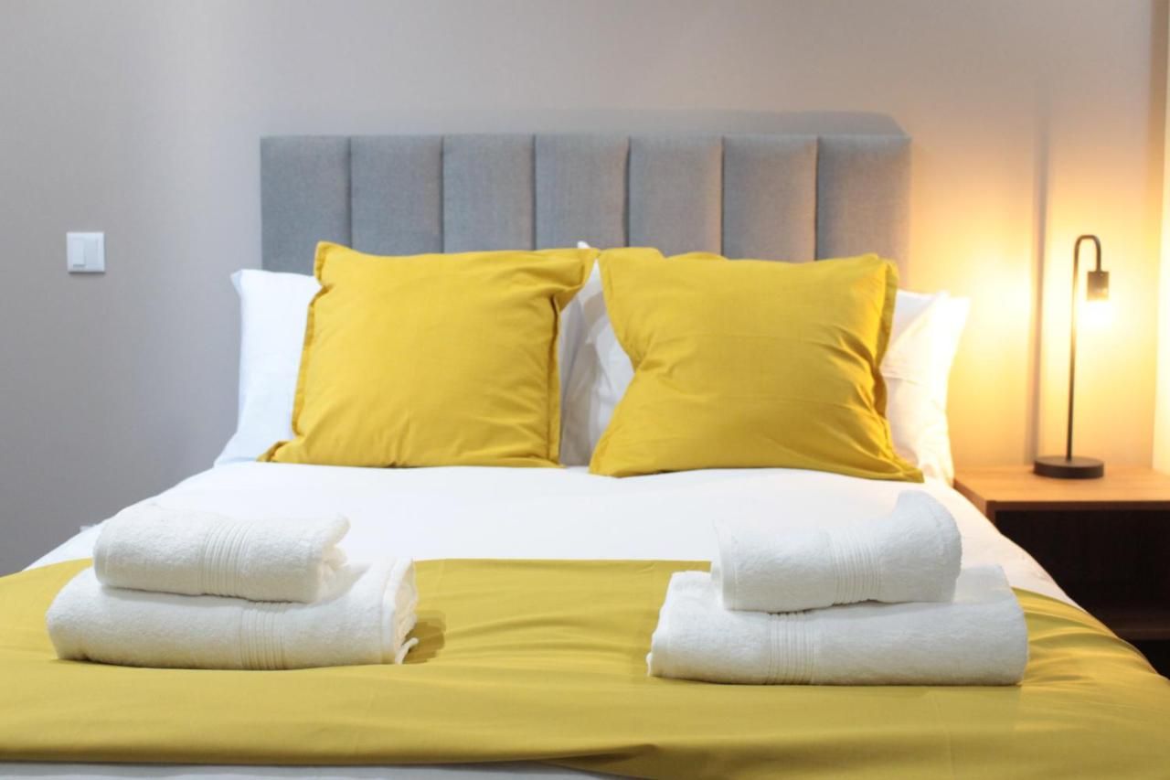 A neatly made bed with white and yellow bedding, a grey headboard, and a bedside lamp.