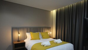 Ein Hotelzimmer mit einem Bett, einem Nachttisch, einer Lampe und einem großen Fenster mit Vorhängen.