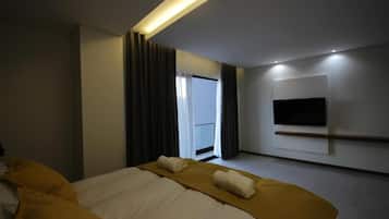 Una habitación de hotel moderna con una cama grande, un televisor de pantalla plana montado en la pared y una ventana con cortinas.