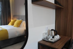 A hotel room with a bed, a bedside table with a tray of breakfast items, and a wall-mounted shelf.