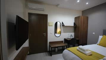 Una habitación de hotel con una cama, un televisor, un escritorio, un espejo y un armario.
