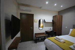 A hotel room with a bed, a TV, a desk, a mirror, and a wardrobe.