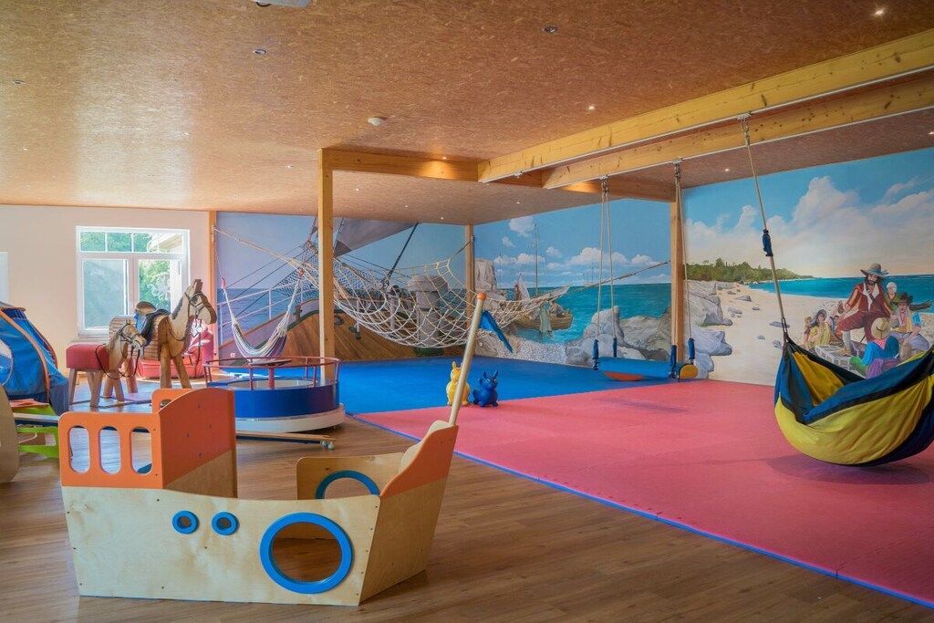 A children's play area with a hammock, a ship-shaped play structure, and a mural of a beach scene.