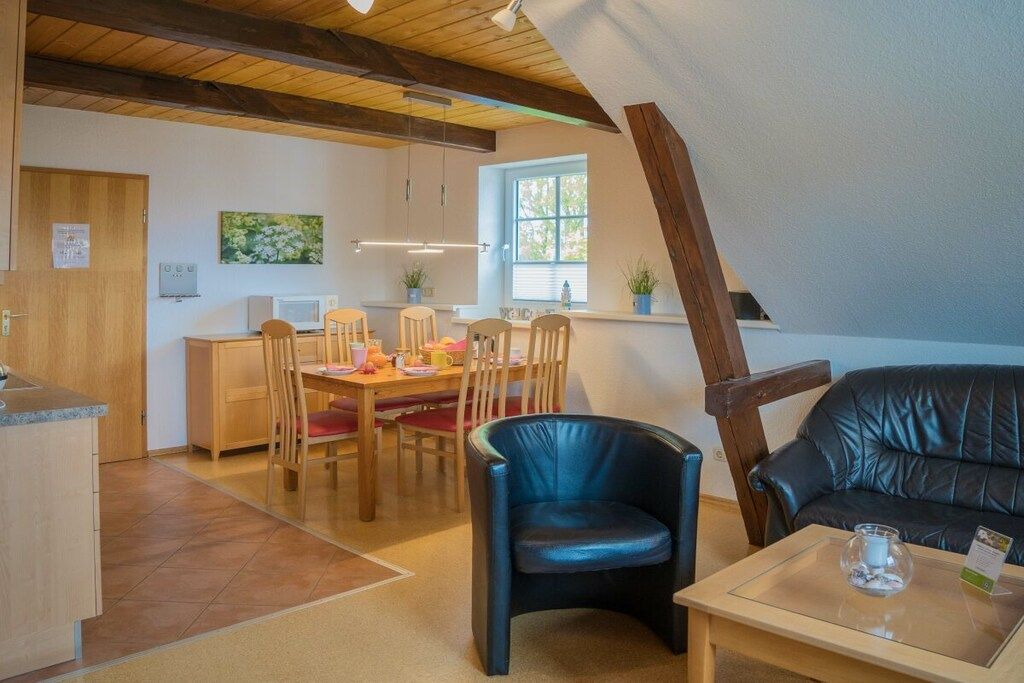 Een gezellige kamer met een zithoek, een zwarte lederen fauteuil, een houten tafel en een raam met uitzicht.