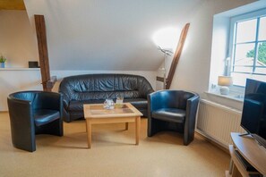 A living room with a sofa, two armchairs, a coffee table, a television, and a window with a view. - Holiday apartment in Fehmarn with Wi-Fi (Fehmarn)