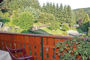 A balcony with a wooden railing overlooking a lush garden and a forested hillside. - Holiday apartment with 2 bedrooms (Schramberg-Tennenbronn)