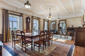 Un'ampia sala da pranzo con un grande tavolo in legno e sedie, un lampadario e vista sull'esterno attraverso ampie finestre.