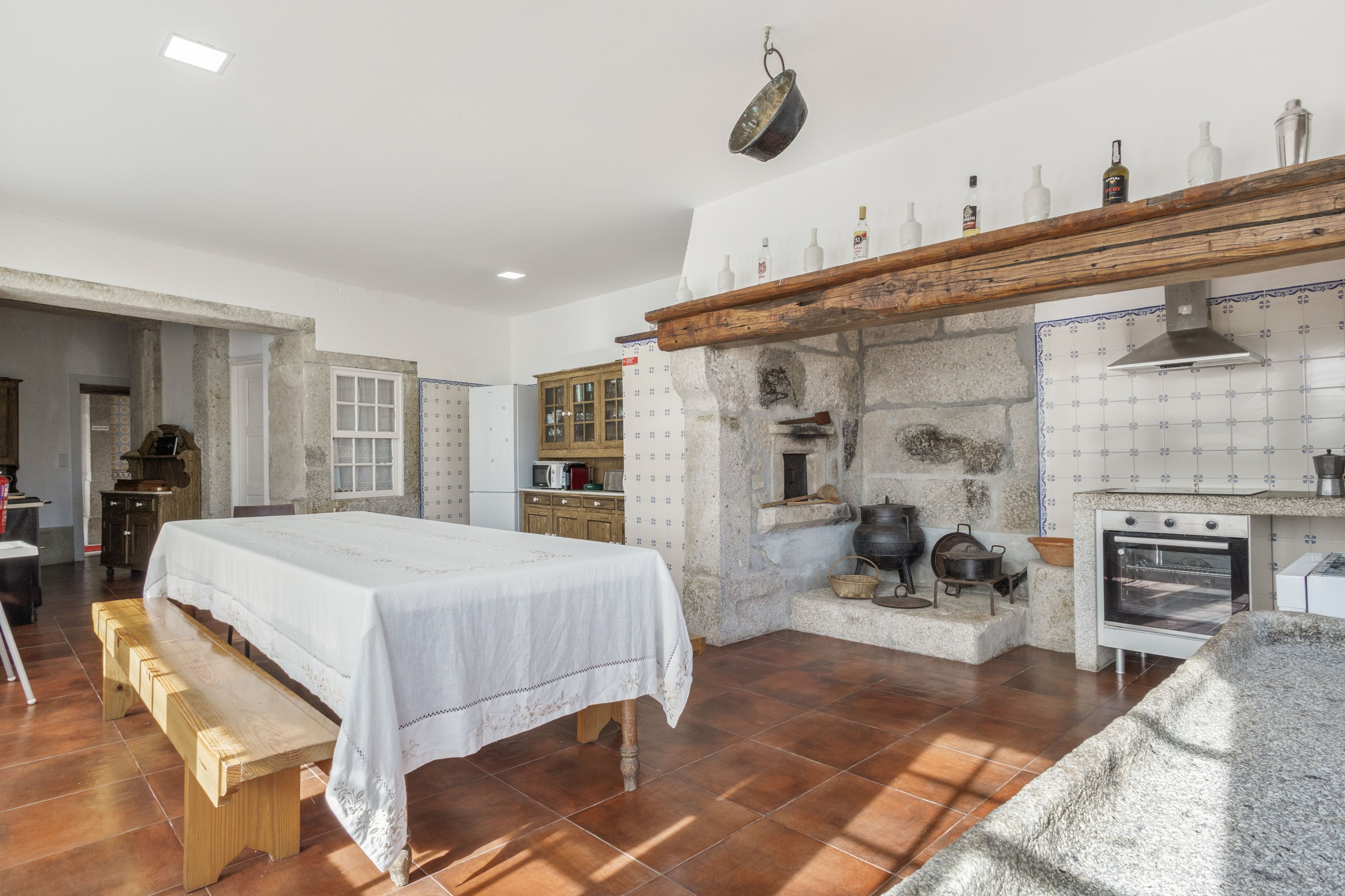A kitchen with a stone wall, wooden cabinets, a hanging pot rack, and a dining area with a bench.