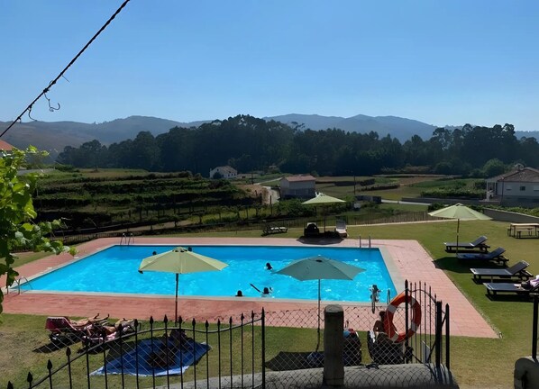 A swimming pool with a fenced area, lounge chairs, and a view of the surrounding landscape.