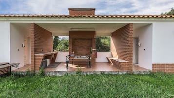 A covered patio area with a brick barbecue grill, a table, and benches.