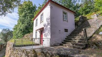 A small, white building with a red door and windows, situated on a stone staircase with a metal railing.
