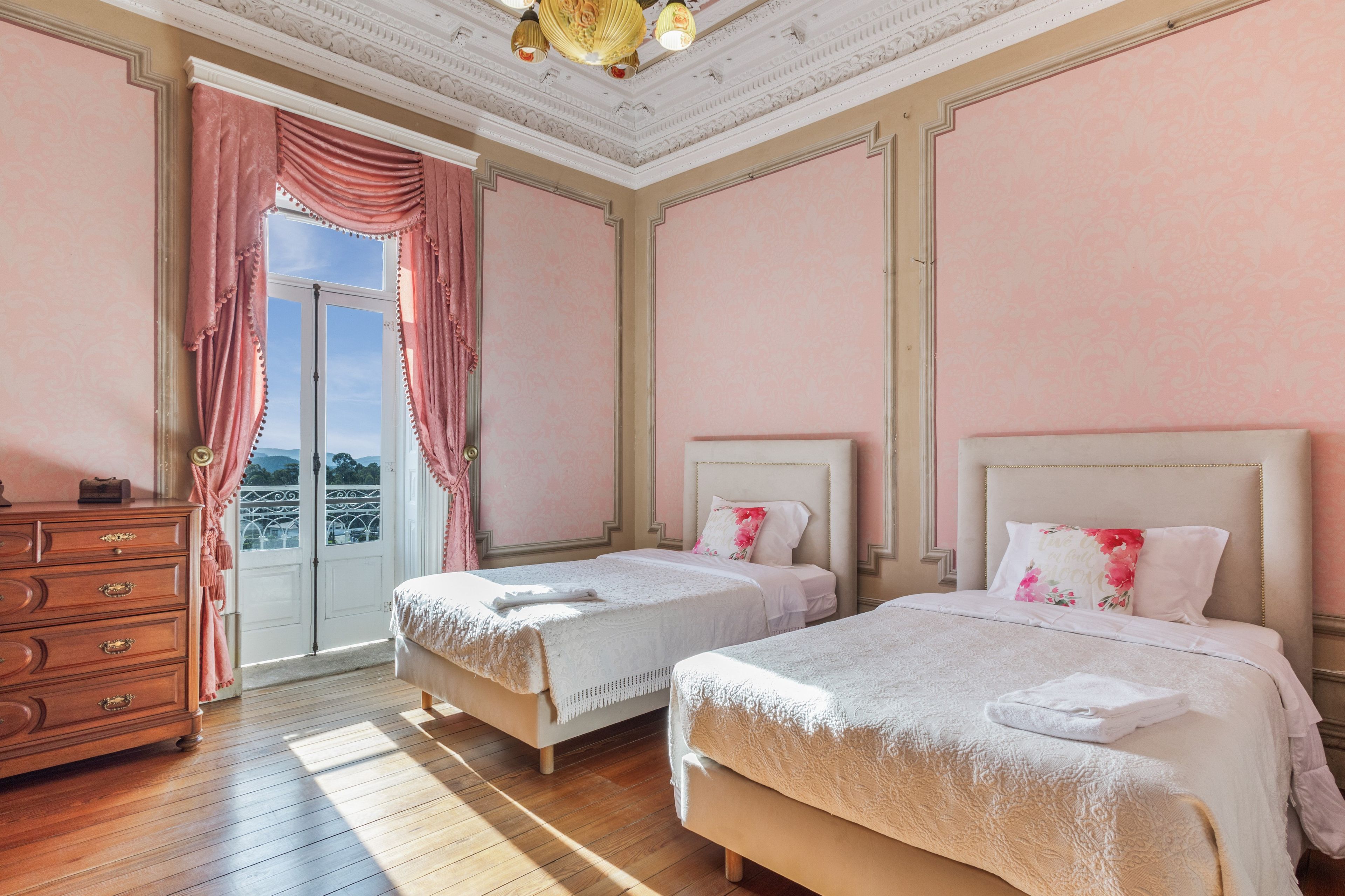 A bedroom with two beds, a dresser, and a large window with curtains.
