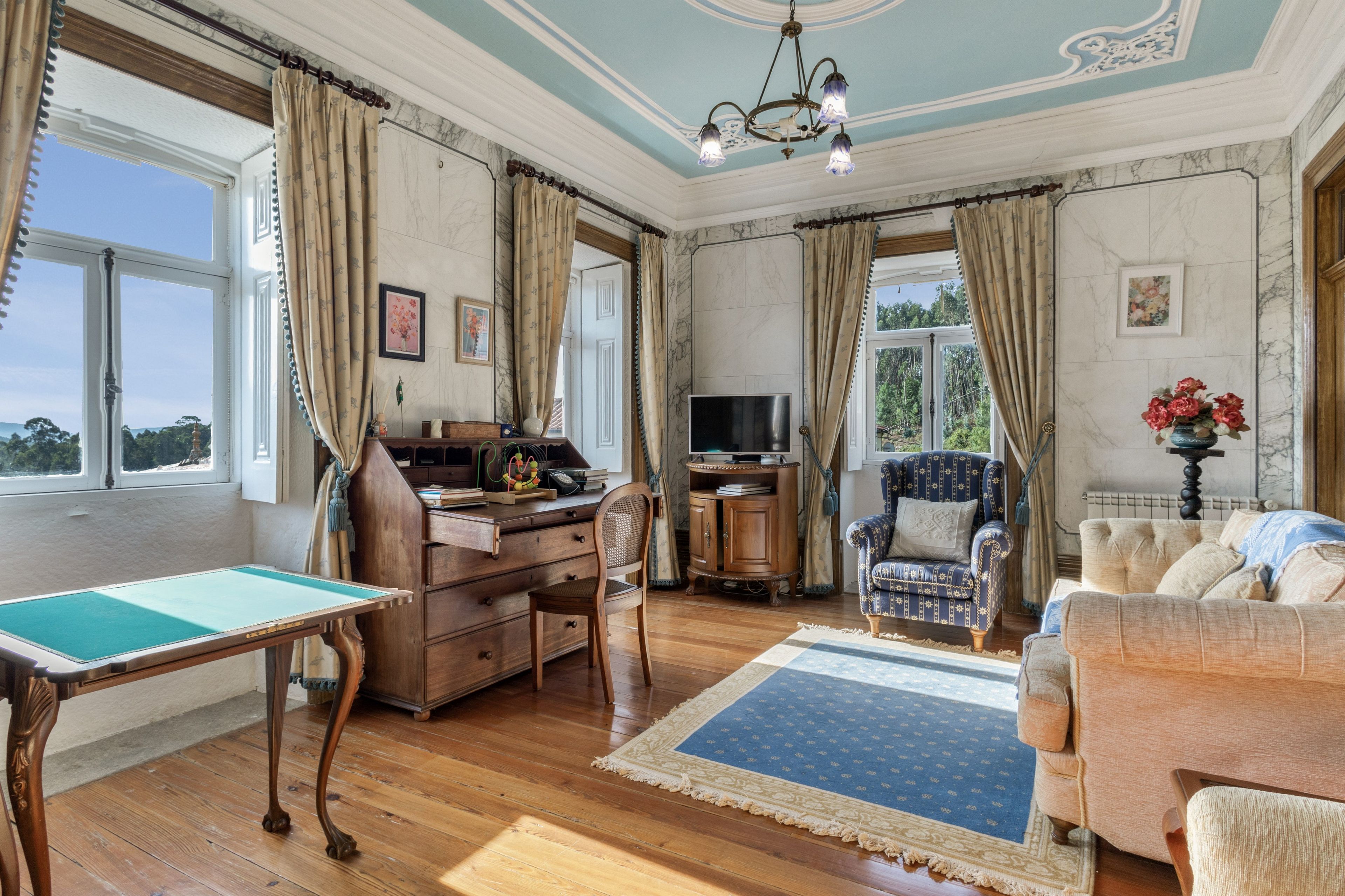 A spacious living room with a wooden floor, a desk, a television, a patterned rug, and a sofa.