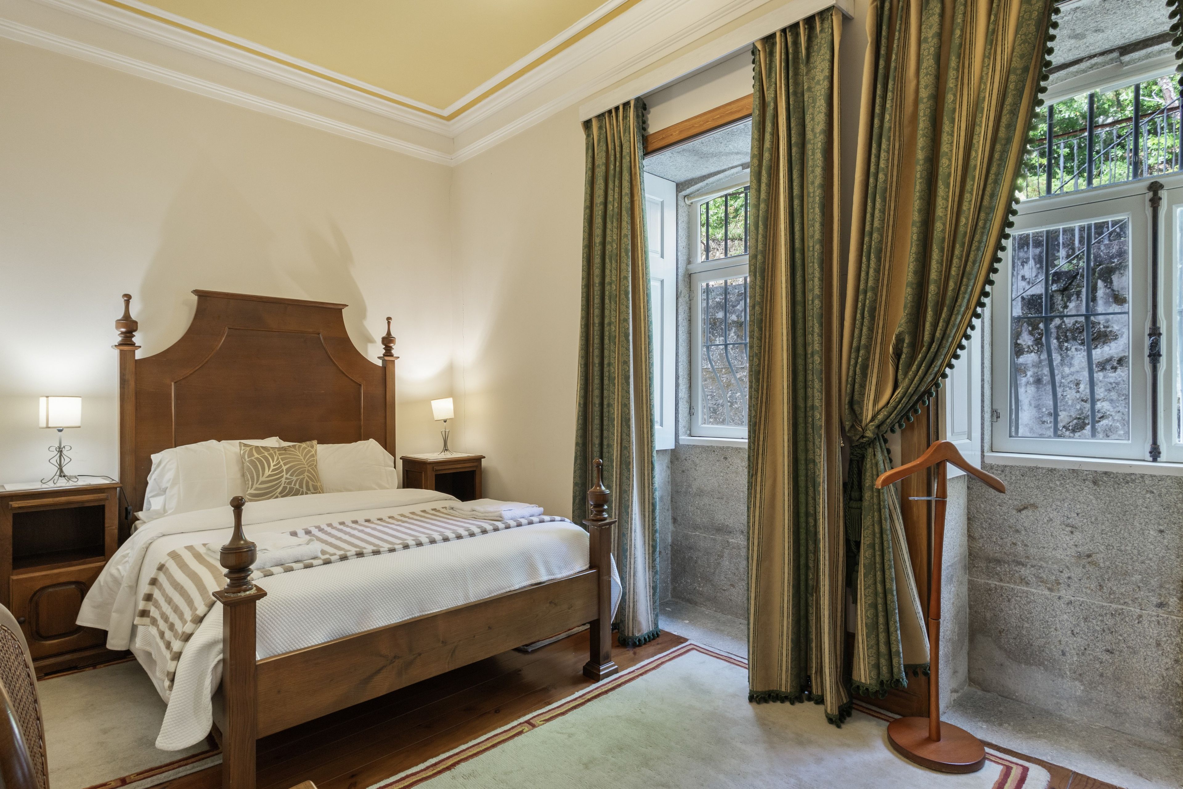 A hotel room with a large bed, two bedside tables with lamps, a window with curtains, and a wooden floor.