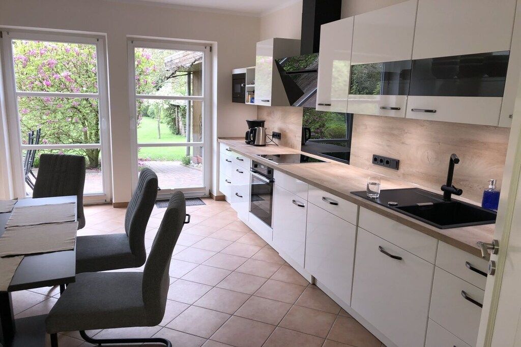 A modern kitchen with white cabinets, a black countertop, and a window overlooking a garden.