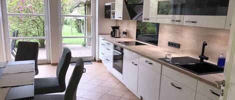 A modern kitchen with white cabinets, a black countertop, and a window overlooking a garden.