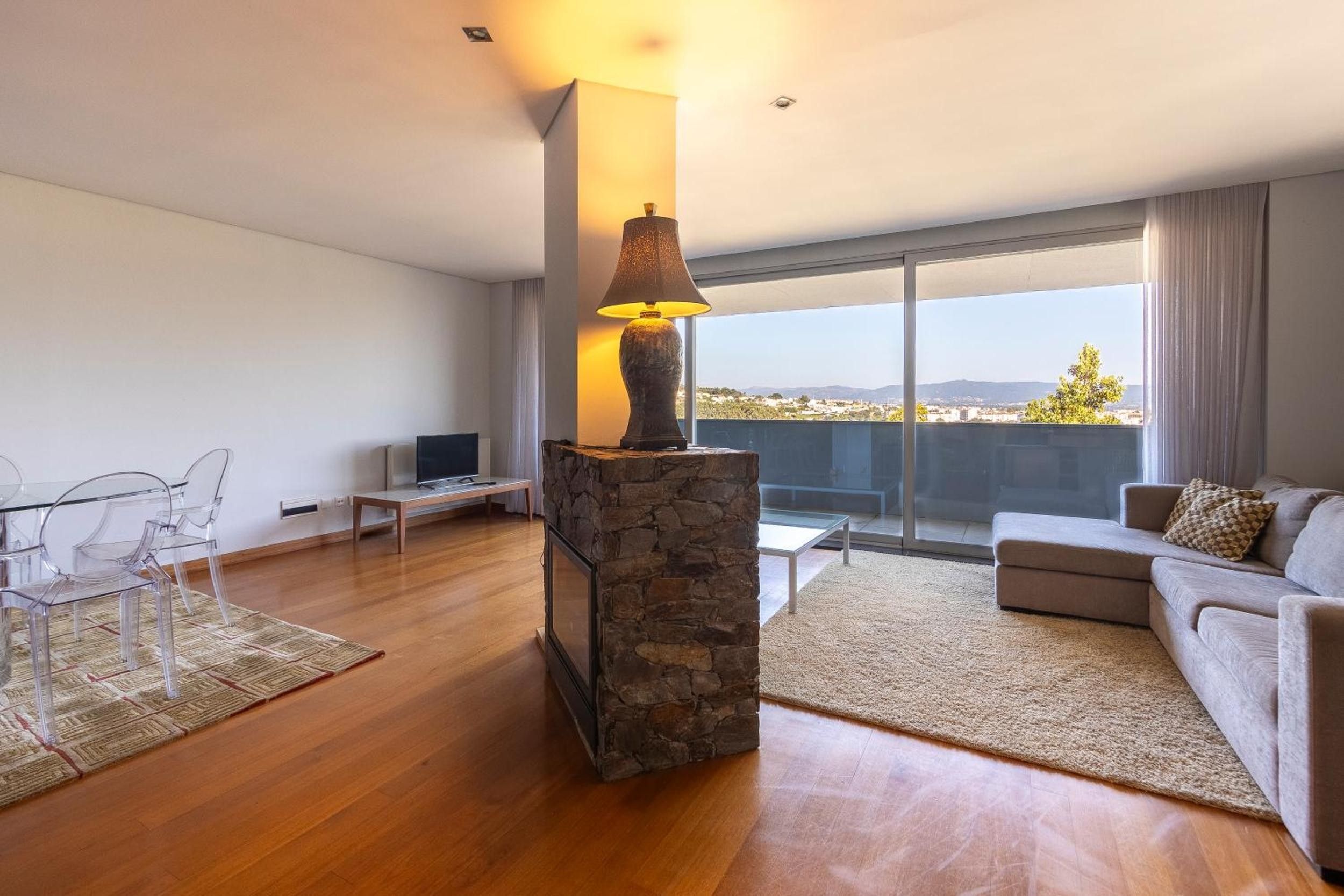 Una sala de estar moderna con chimenea de piedra, una mesa de centro de vidrio, un sofá y vistas de la ciudad.