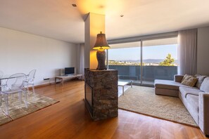 A modern living room with a stone fireplace, a glass coffee table, a sofa, and a view of the cityscape. - Villa 'Casa Sao Francisco' with Sea View, Wi-Fi and Air Conditioning (Montanha de Santa Luzia)