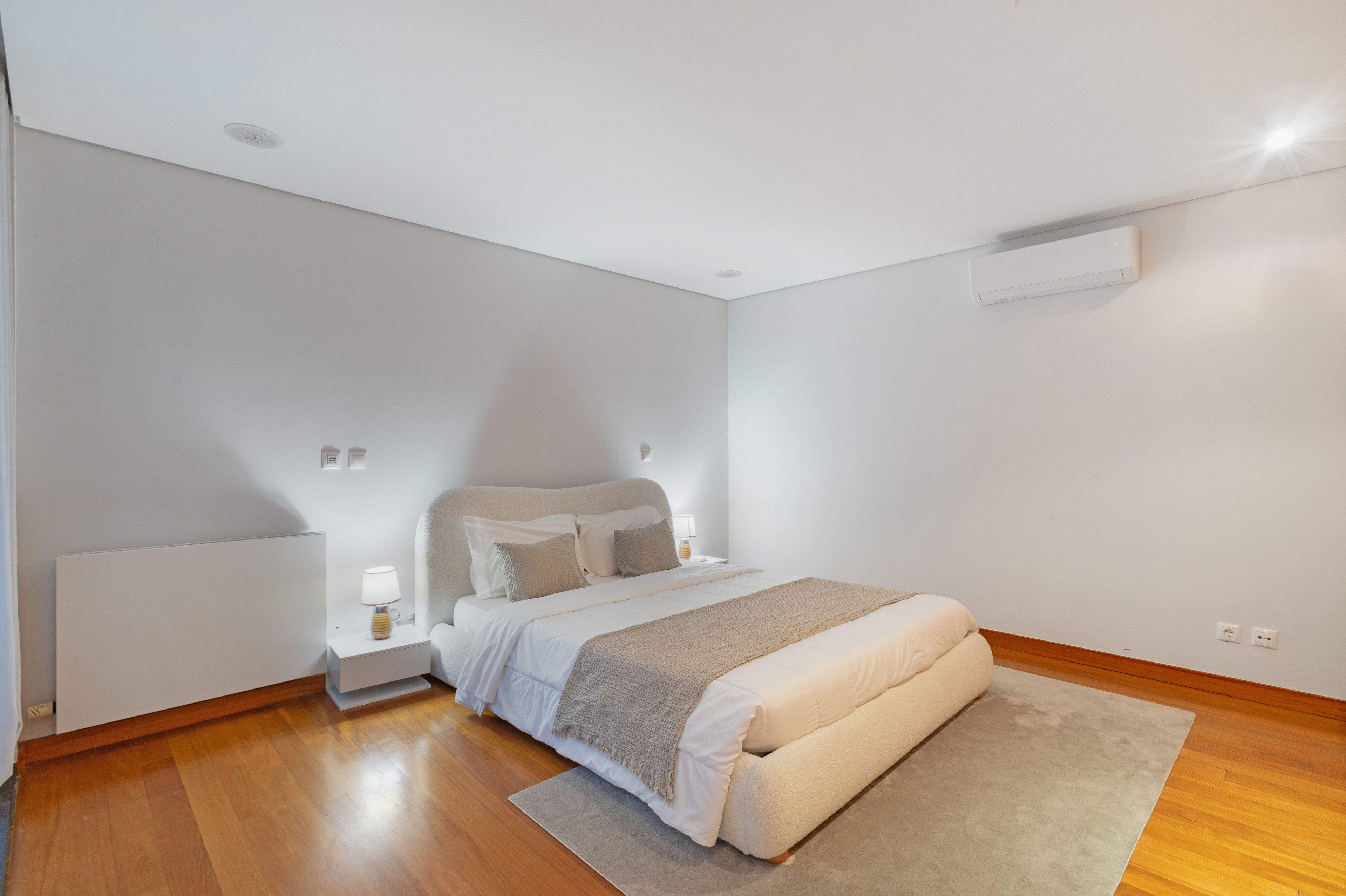 A modern bedroom with a single bed, bedside tables, a radiator, and a ceiling-mounted air conditioner.