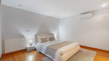 A modern bedroom with a single bed, bedside tables, a radiator, and a ceiling-mounted air conditioner.