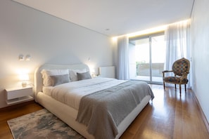 A modern bedroom with a large bed, a chair, and a view of the outdoors.