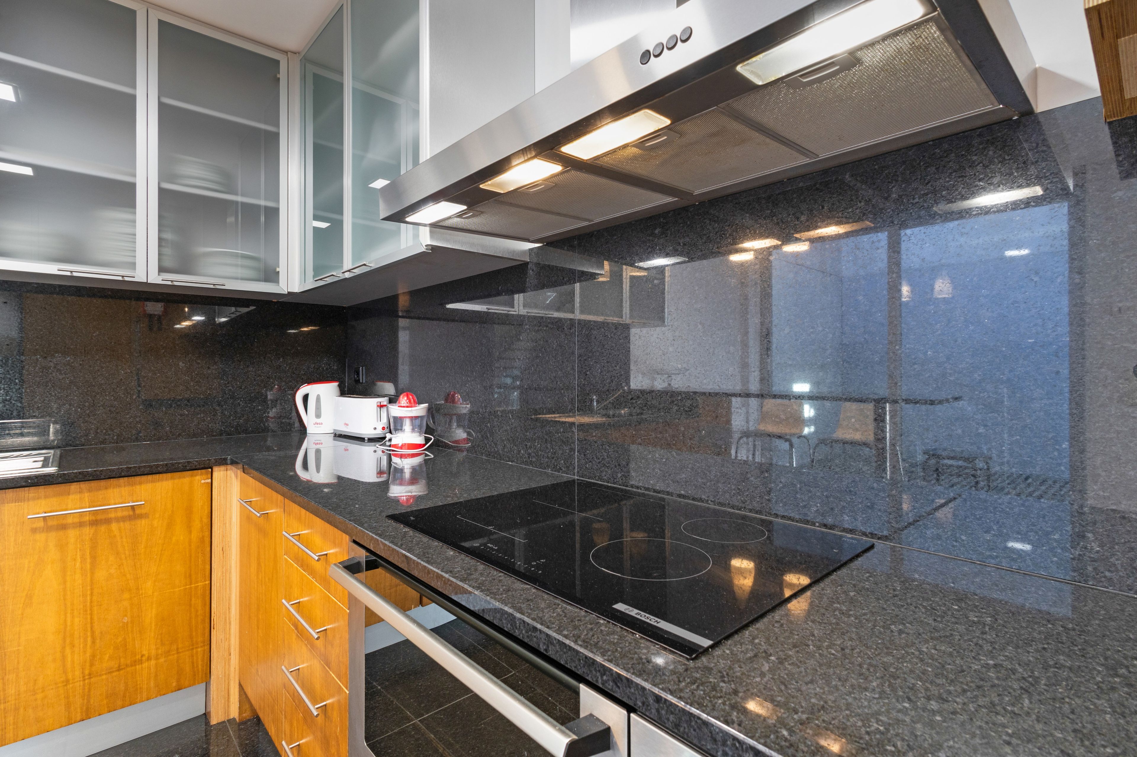 Une cuisine moderne dotée d’un plan de travail noir, de meubles en bois et d’une plaque de cuisson à induction de la marque Bosch.