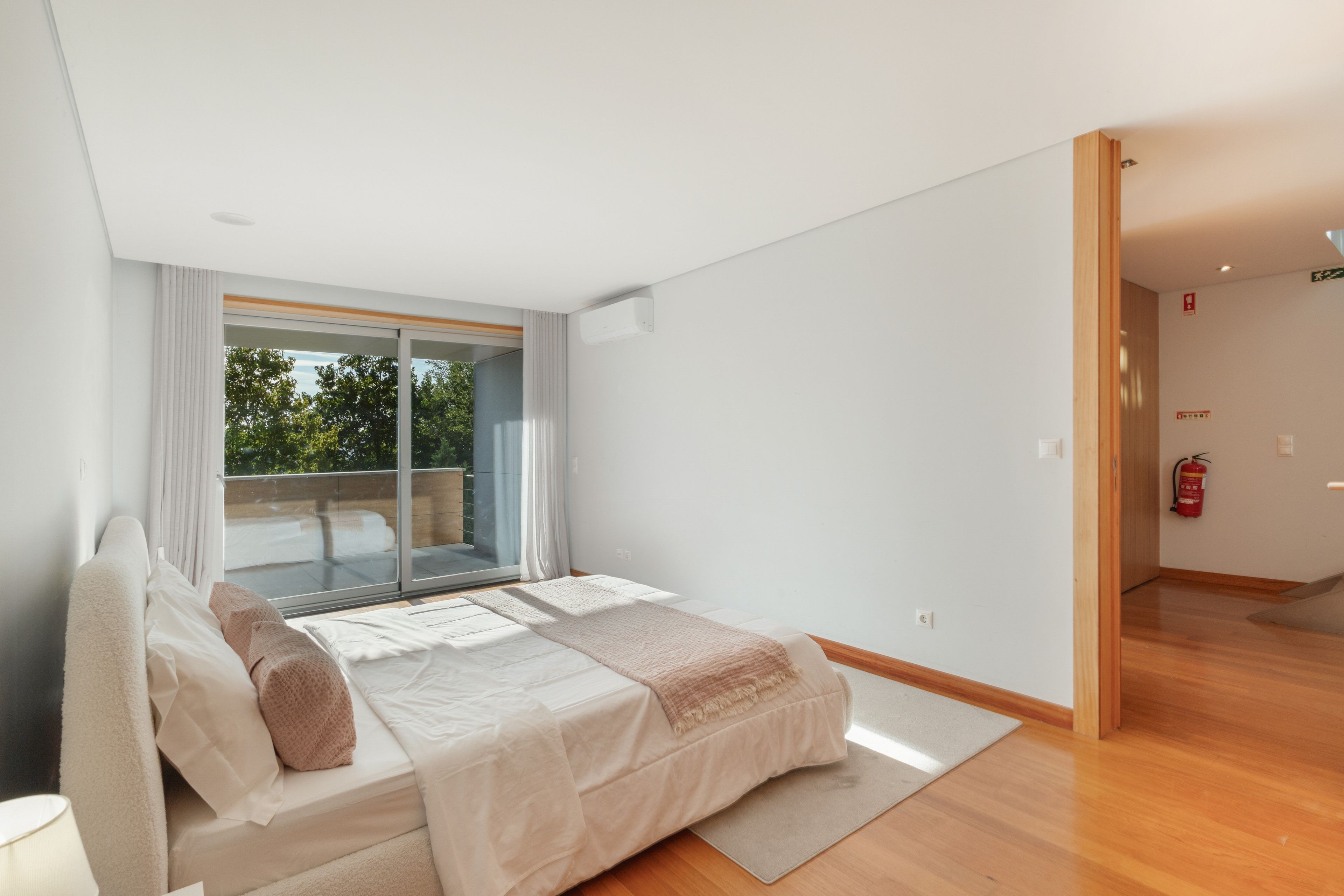 A bedroom with a large bed, a sliding glass door to a balcony, and a fire extinguisher on the wall.
