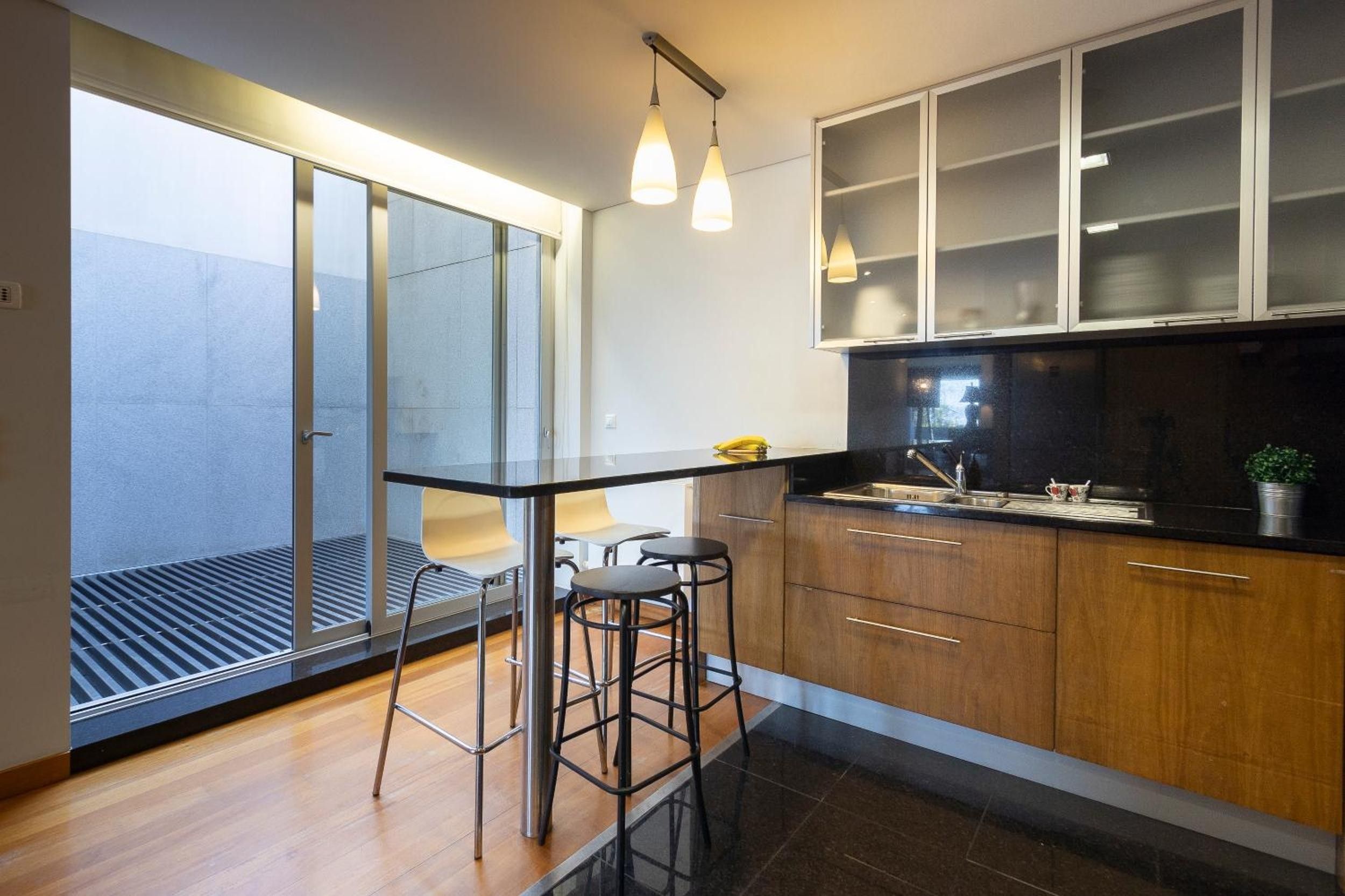 Una cocina moderna con encimera negra, armarios de madera y puerta de vidrio que da a un balcón.