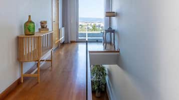 Un interno moderno con pavimento in legno, una scala, vista attraverso una porta vetrata e un piccolo tavolo con lampada.