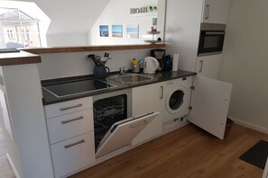 Een compacte keuken met een vaatwasser, wasmachine en magnetron.