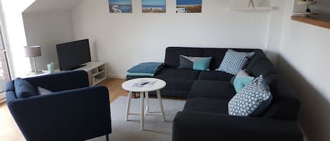 A modern living room with a sofa, armchair, and a television on a stand.