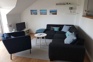 Een moderne woonkamer met een bank, fauteuil en een televisie op een dressoir.