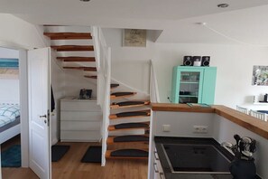 Een moderne keuken met een inbouwfornuis, een blauwgroen kastje en een trap naar een slaapkamer.