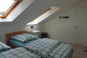 A bedroom with a sloped ceiling, a bedside table with a lamp, a trash bin, and a door with a small decorative item above it. - Holiday apartment with 2 bedrooms (Schönhagen)