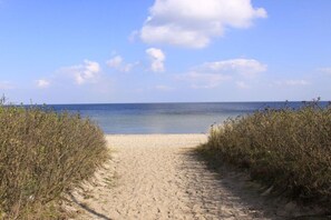 Een zandpad langs het strand naar de zee, onder heldere luchten.