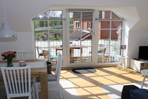 Une pièce avec une grande fenêtre, une table en bois, une chaise blanche et un téléviseur.