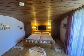 A bedroom with a wooden ceiling, a bed with a TV above it, and a window with curtains. - Mariele holiday apartment (Ettal)