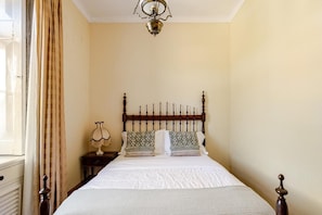 A bedroom with a bed, a nightstand, a lamp, and a window with curtains.