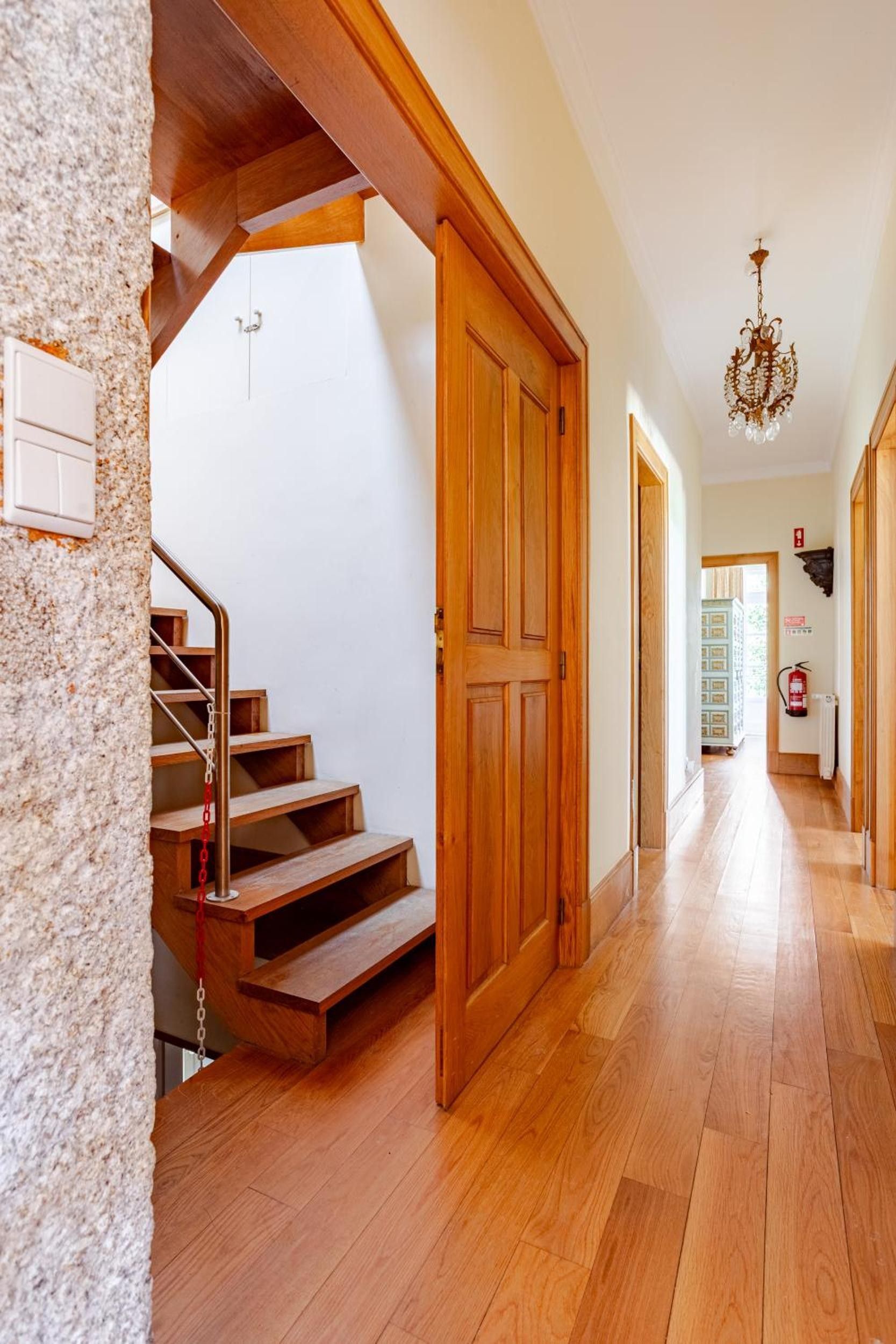 A wooden staircase leading to a landing, a hallway with wooden flooring, and a chandelier.