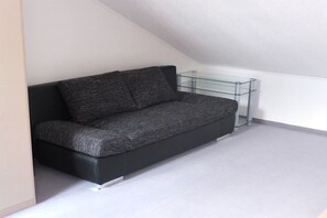 Un canapé noir est placé dans un coin d’une pièce, avec une étagère en verre adossée au mur.