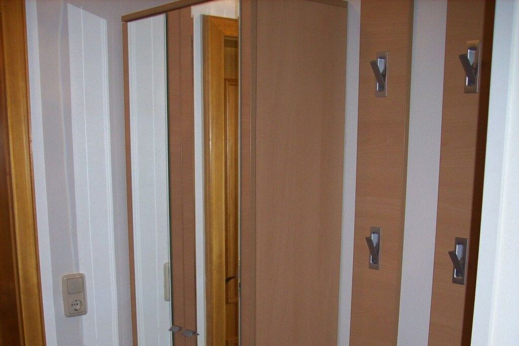 A hotel room with a wooden door, a mirror, and a light switch on the wall.