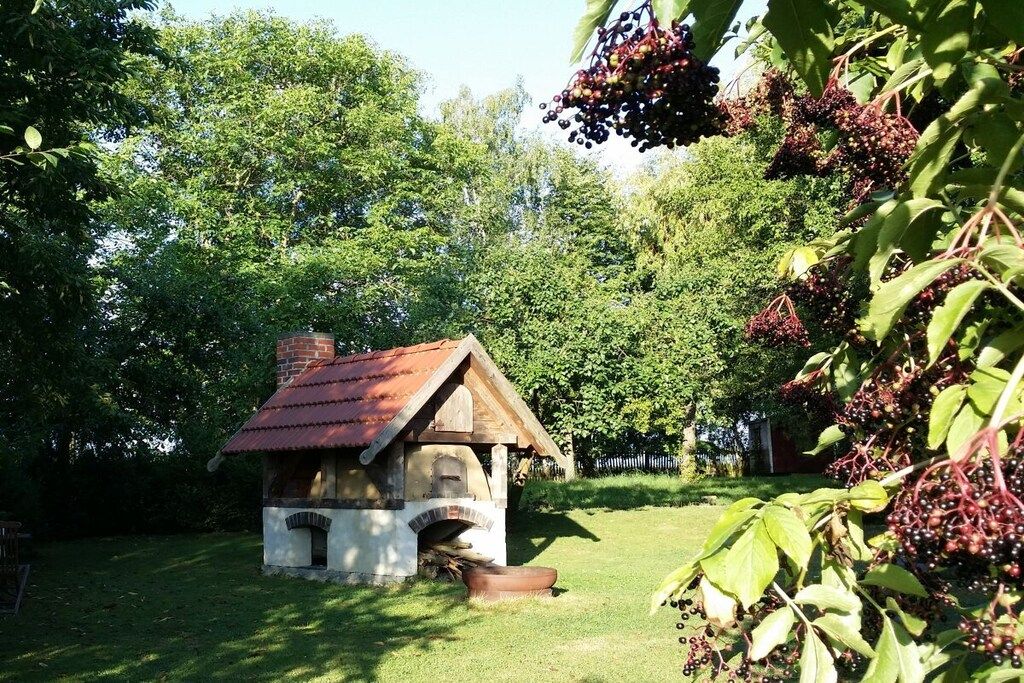 Ein rustikales Holzgebäude mit geneigtem Dach, möglicherweise eine Scheune oder ein kleines Haus, umgeben von üppigem Grün und Bäumen.