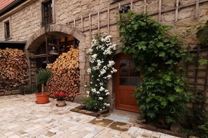 A stone building with a wooden door, a stack of firewood, and a climbing white flower wall. - Holiday apartment with 5 bedrooms (Rathmannsdorf)