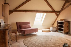 A loft bedroom with a sloped ceiling, a wooden dresser, a pink chair, a woven rug, and a skylight. - Holiday apartment with 5 bedrooms (Rathmannsdorf)