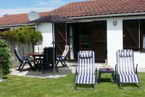 A patio with a table and chairs, two striped lounge chairs, and a satellite dish on a house with a tiled roof. - Zeewind Bredene - Belgian coast (Bredene)